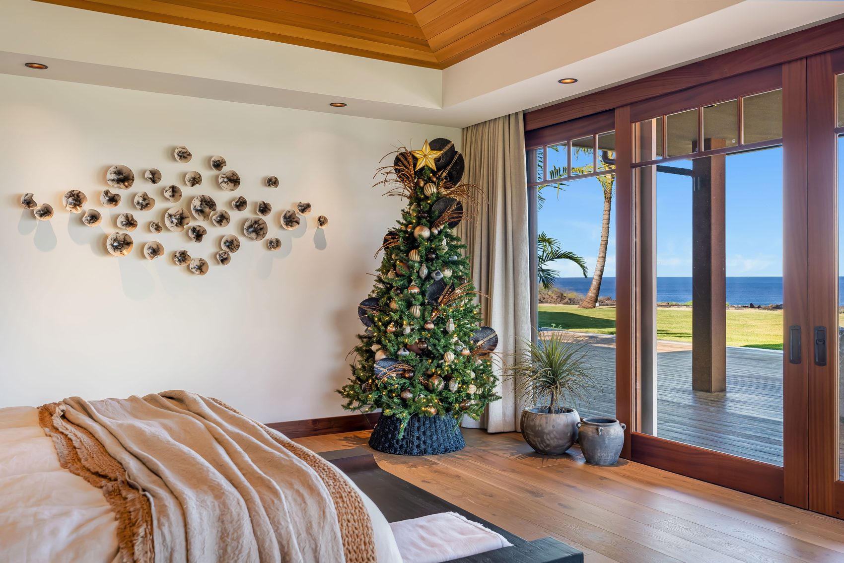 Coastal holiday bedroom. A natural gold-and-green holiday tree complements the room’s warm woods and ocean views.